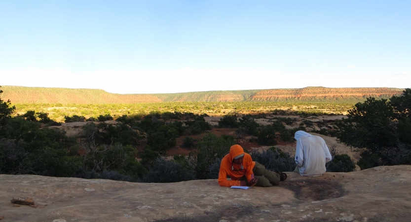 Two people sit on a rock overlooking a desert landscape and journal.